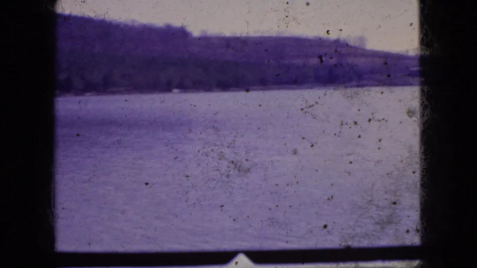 1966 New Jersey 8mm frame with a wide lake, dark wooded hillside, pale sky, dust marks, and heavy black scan borders.