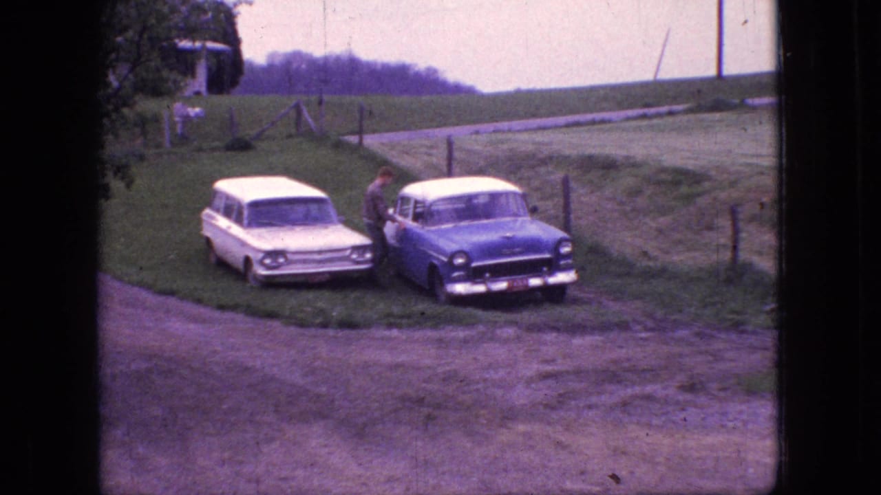 1966 New Jersey 8mm frame showing a white station wagon and a blue-and-white sedan parked beside a rural dirt road, with a man standing at the sedan.