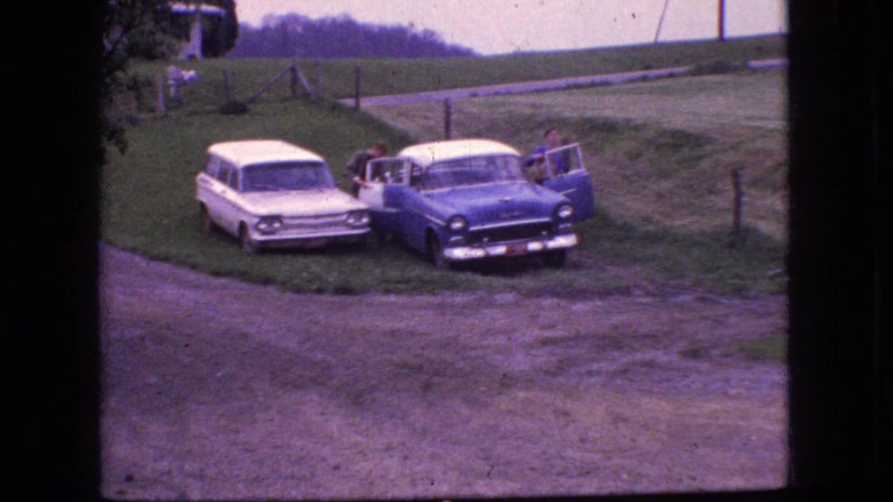 1966 New Jersey 8mm frame showing the two parked cars from a rural roadside angle, with a person leaning near the blue sedan and the door open.