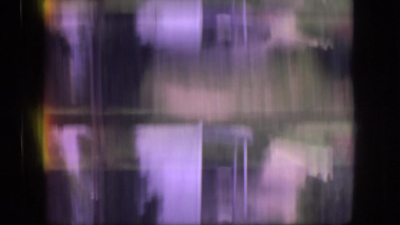 Soft, motion-blurred 8mm frame with vertical streaking and indistinct outdoor forms during a transition between scenes.