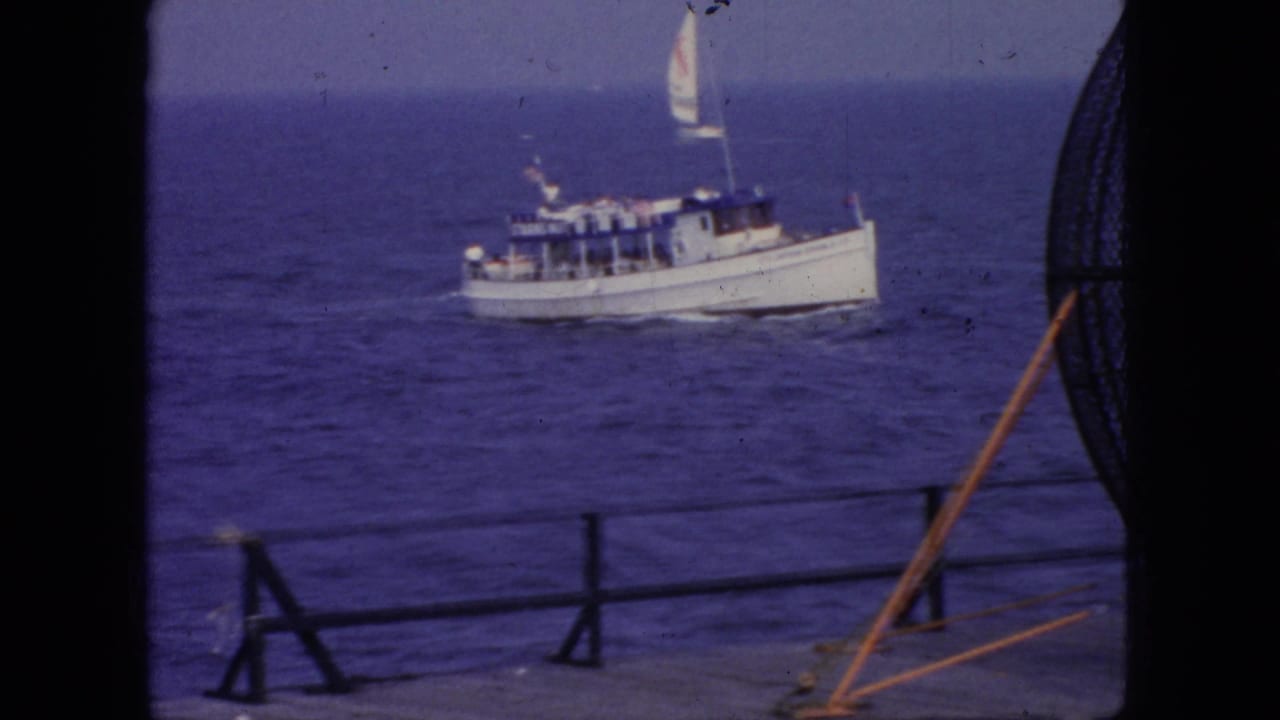 A small white motorboat with a raised sail or mast detail moves across blue water off the New Jersey coast in this 1966 8mm home-movie frame.