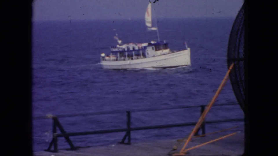 A small white motorboat with a raised sail or mast detail moves across blue water off the New Jersey coast in this 1966 8mm home-movie frame.