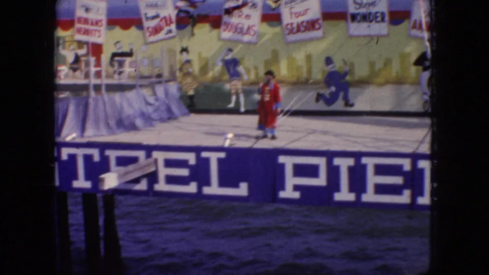 A pier stage show scene in 1966 New Jersey shows a red-costumed performer in front of painted signage and backdrop names, with distant figures on the stage area.