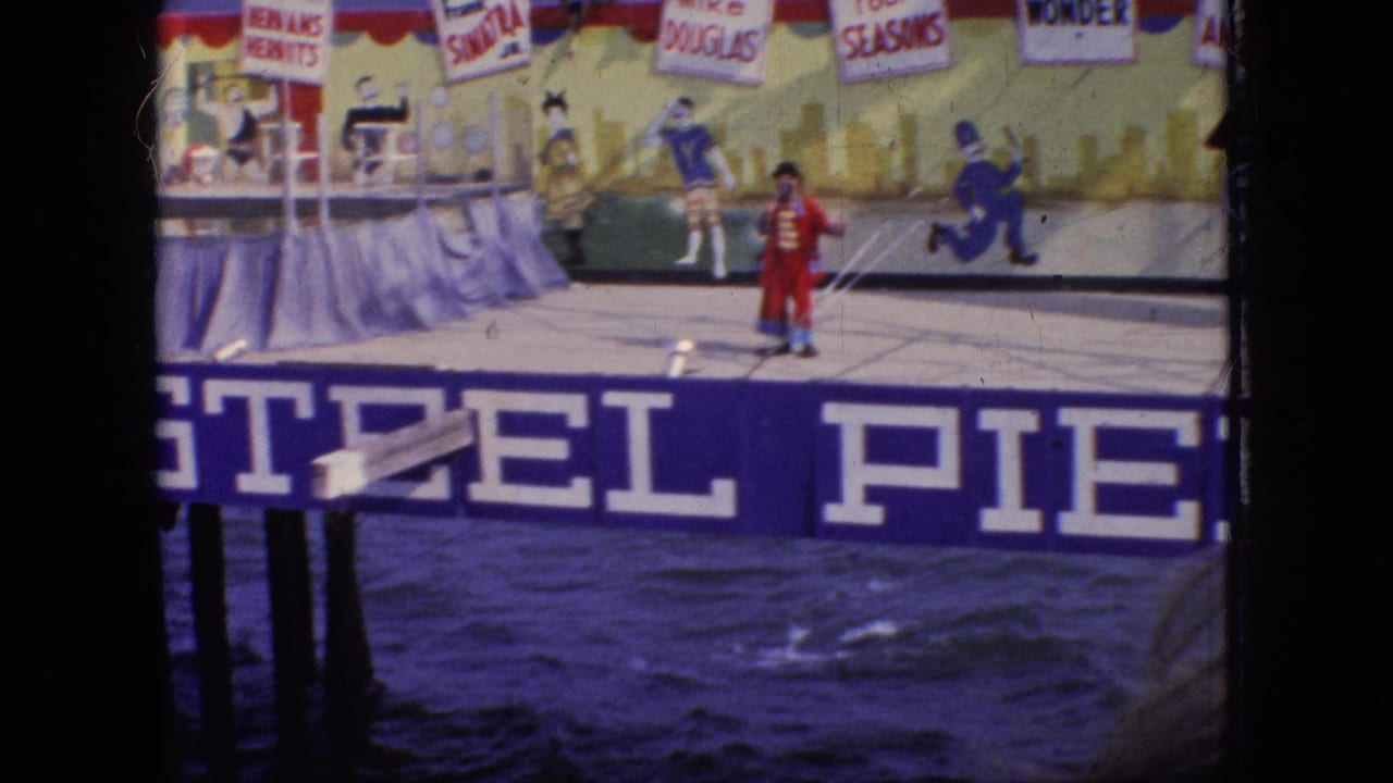 Red-coated performer stands near the center of a pier stage with water below and hanging signs above.