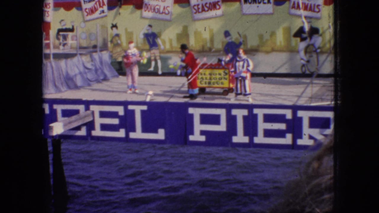 1966 New Jersey home-movie frame showing clown-costumed performers on a Steel Pier stage with a painted entertainment backdrop and water in the foreground.