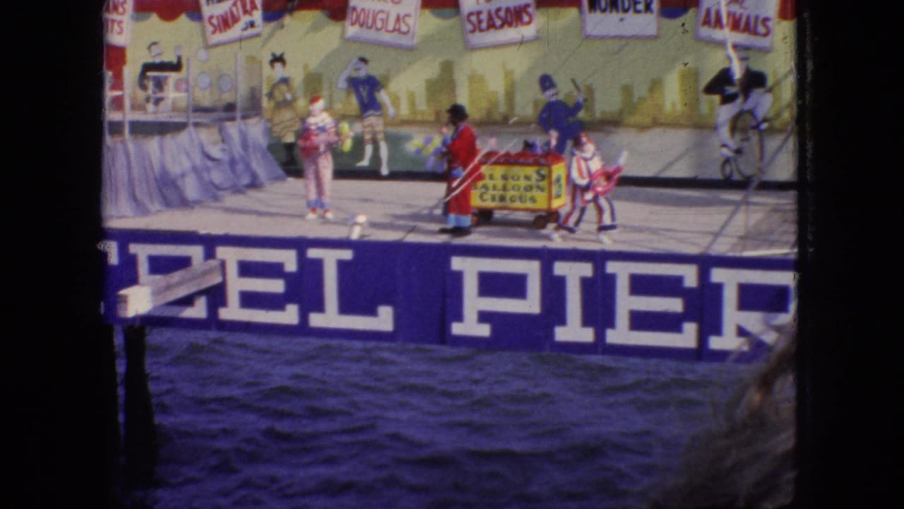 1966 New Jersey frame of a comic pier-stage act with clown-costumed performers near a small cart and Steel Pier signage visible below.