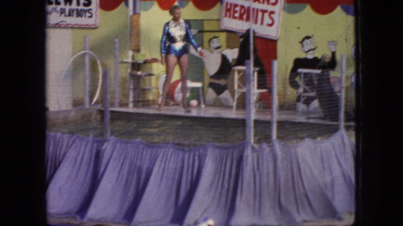 Performer stands on a decorated stage beside a pool with band-name signs behind her.
