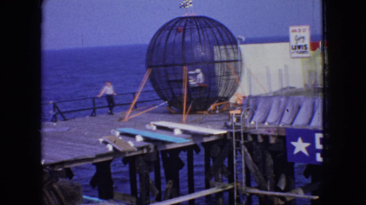 1966 New Jersey 8mm frame showing the large spherical cage from a wider pier angle, with ocean in the background, a nearby man, stage platforms, curtains, and partial signage.