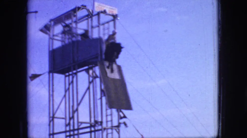 New Jersey 1966 pier circus frame showing a performer with an animal or mount on a tall metal stunt tower, seen against a pale sky with rigging lines visible.