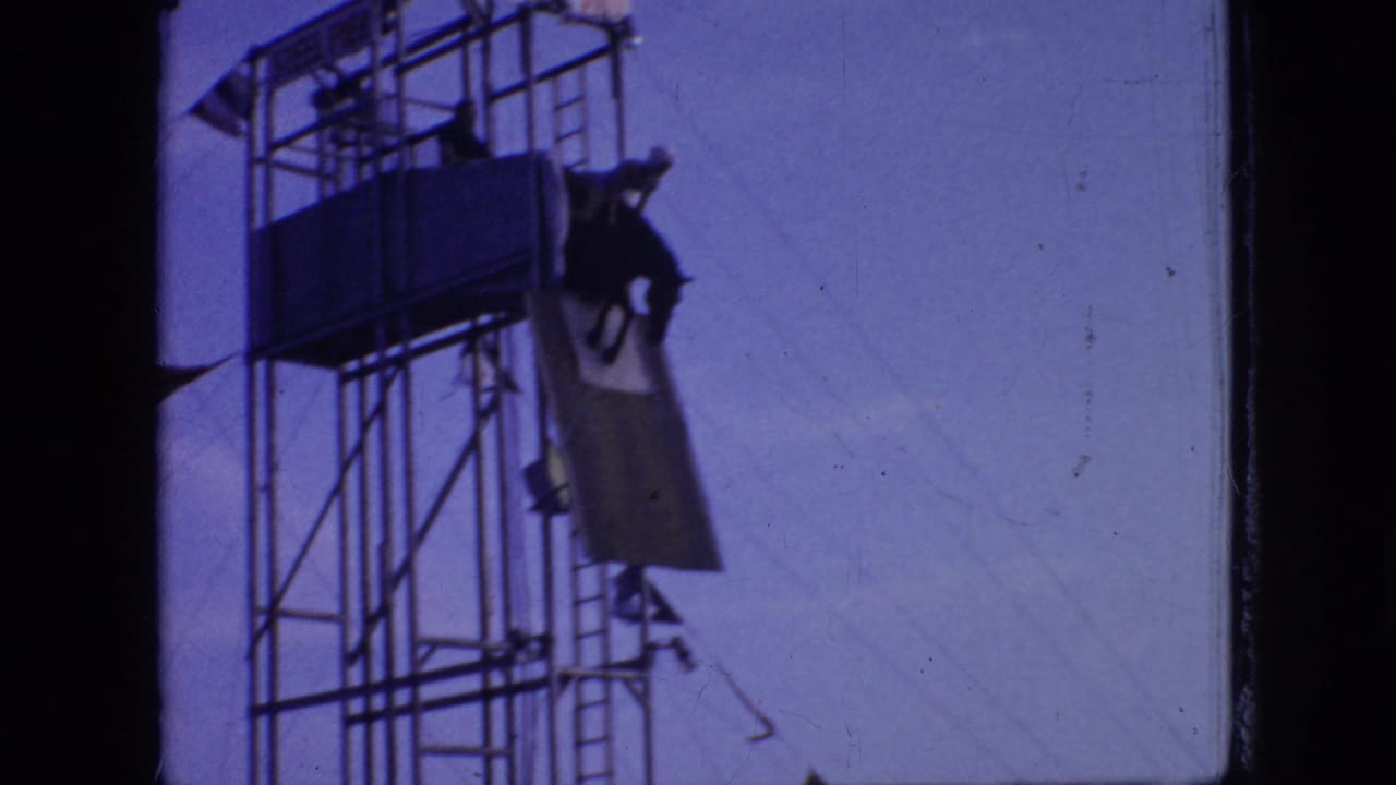 In this 1966 New Jersey Super 8 frame, a horse and rider appear silhouetted near the upper platform of a tall metal scaffold used for an oceanfront dive stunt.