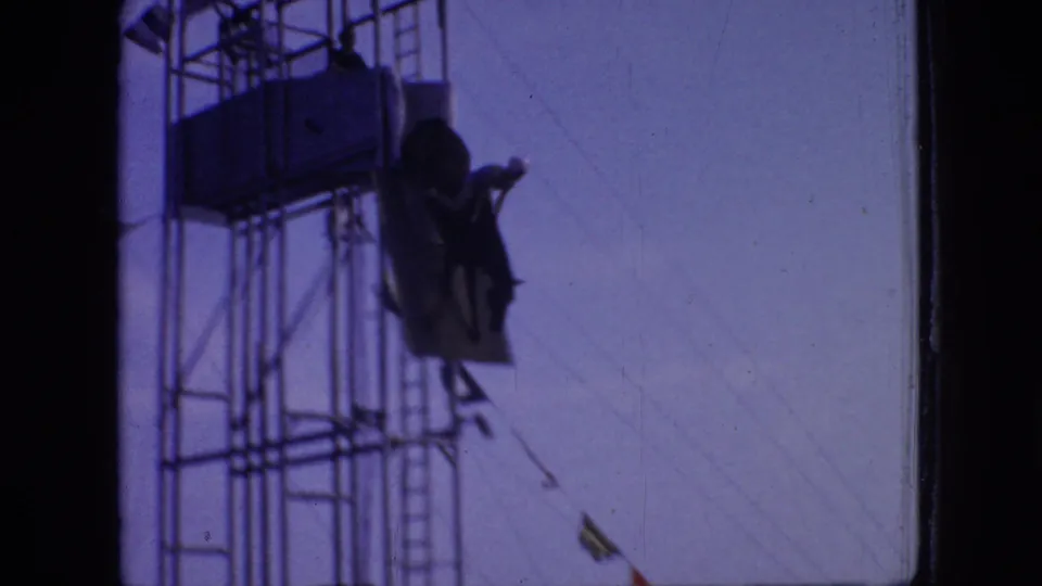 The horse and rider are seen mid-descent from the elevated scaffold, with the sloped ramp and steel tower silhouetted against the sky.