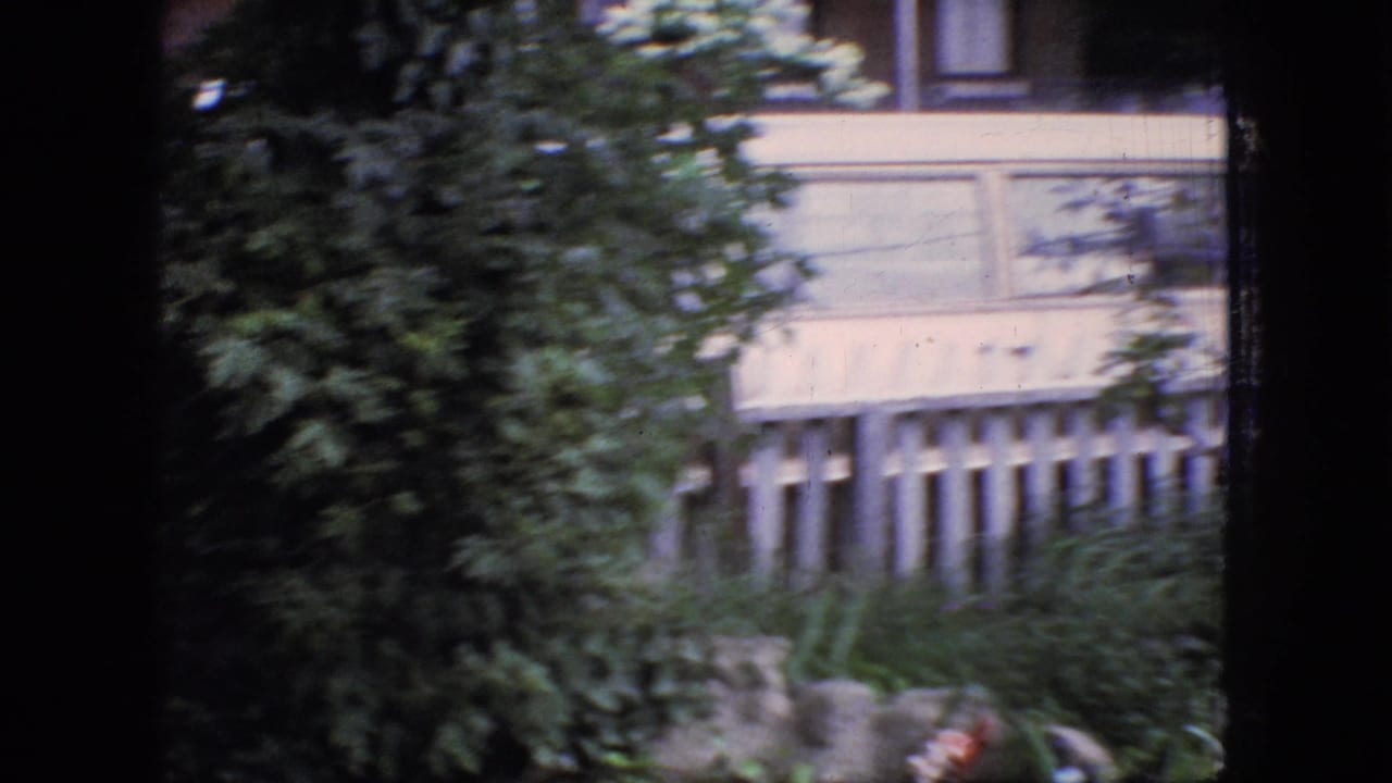 1966 New Jersey 8mm frame showing a house exterior, white picket fence, and dense foliage from a window-framed home-movie perspective.