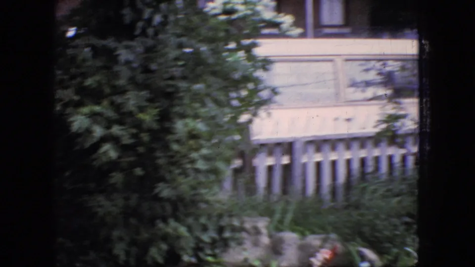 1966 New Jersey 8mm frame showing a house exterior, white picket fence, and dense foliage from a window-framed home-movie perspective.