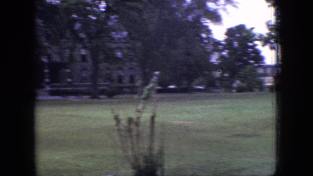 1966 New Jersey 8mm frame showing a grassy lawn, mature trees, and distant brick buildings divided by a dark interior window frame.