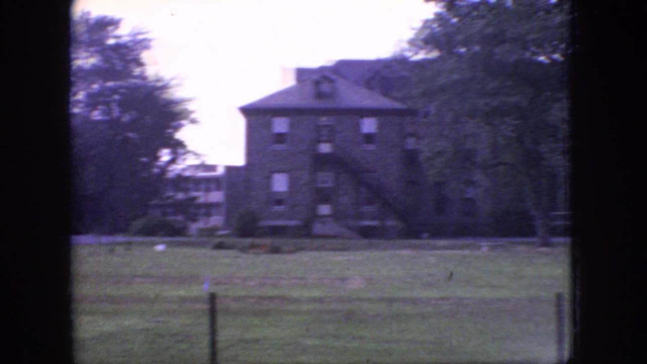 1966 New Jersey 8mm frame showing a large brick house-like building with an exterior staircase, lawn, trees, and distant structure at left.