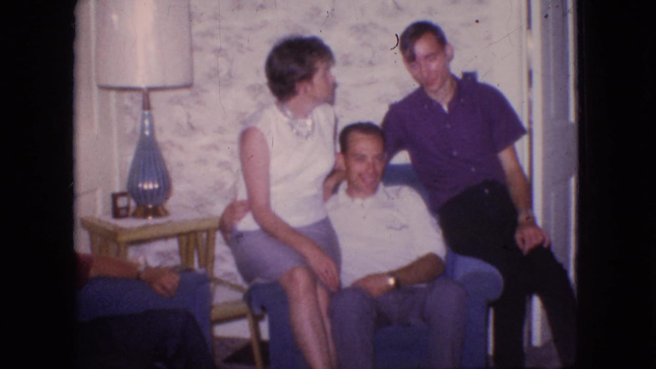 In the final 1966 New Jersey frame, the woman turns toward the standing man as the seated man rests in the blue armchair, with a side table, blue glass lamp, wallpaper, and open door visible.