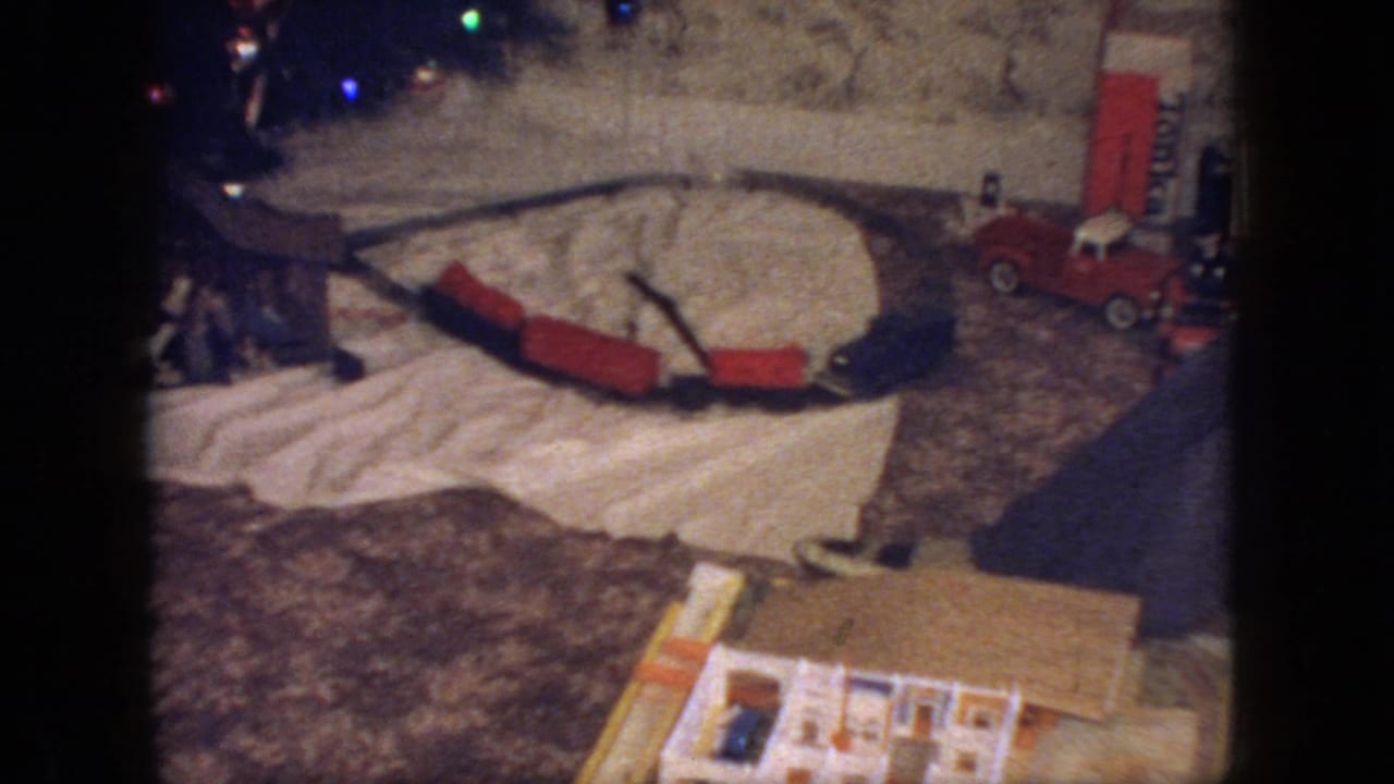 1966 New Jersey interior frame with a toy train layout, red train cars, a red toy truck, and colored Christmas lights visible around the base of the tree.