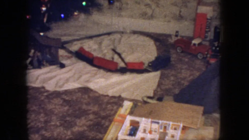 1966 New Jersey interior frame with a toy train layout, red train cars, a red toy truck, and colored Christmas lights visible around the base of the tree.