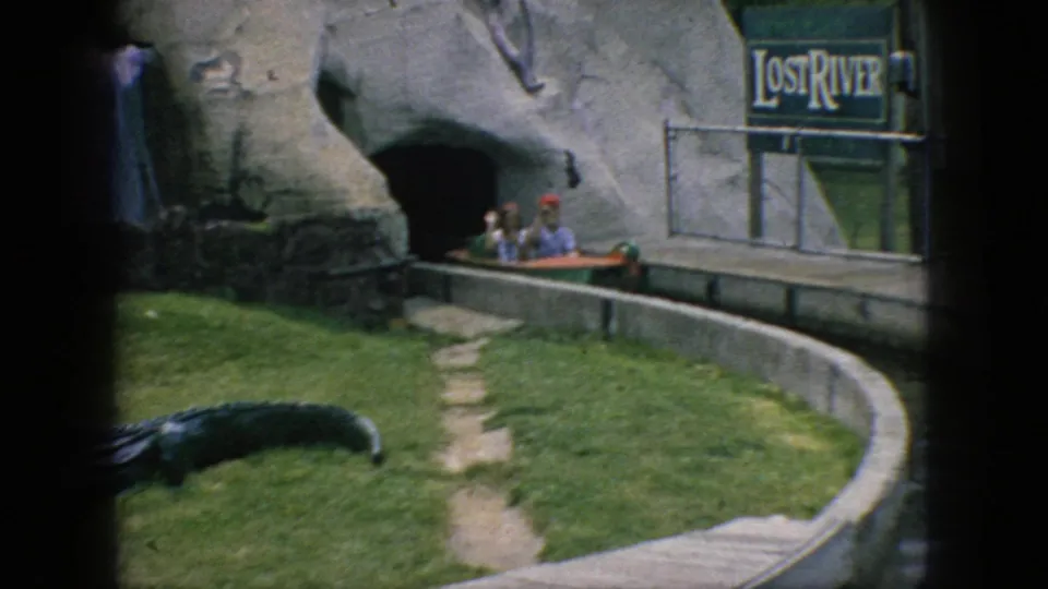1966 New Jersey 8mm frame showing a small amusement-ride boat with distant passengers moving along a curved water channel beside the Lost River sign and themed cave facade.