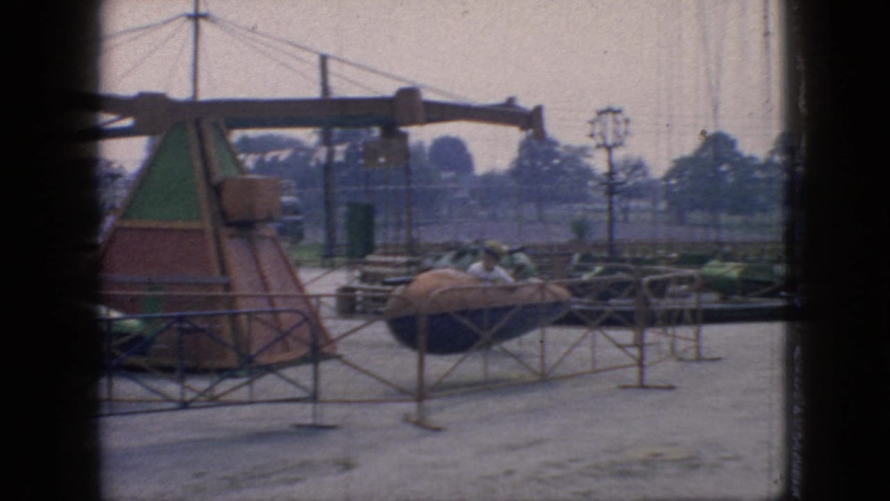 1966 New Jersey 8mm frame showing a spinning amusement ride with green and brown pods, metal railings, utility poles, and dark vertical framing from the camera position.