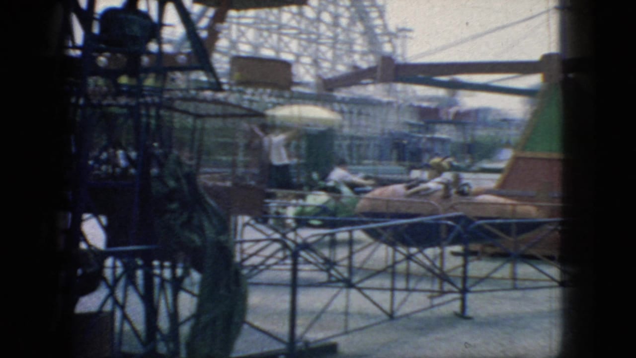 1966 New Jersey 8mm frame of a rotating amusement-park ride structure with pod cars, metal supports, railings, and a distant coaster-like framework.