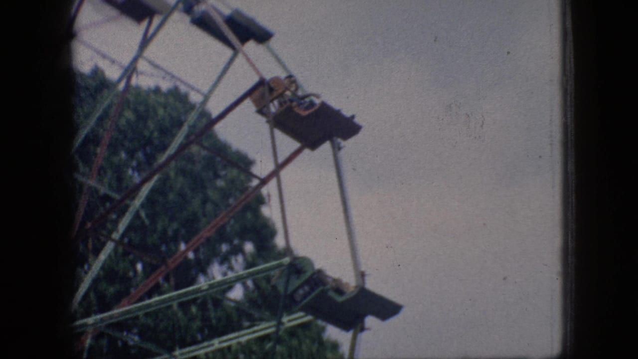 1966 New Jersey home-movie frame showing part of a Ferris wheel with suspended seats, riders at a distance, trees, pale sky, and dark film-edge borders.