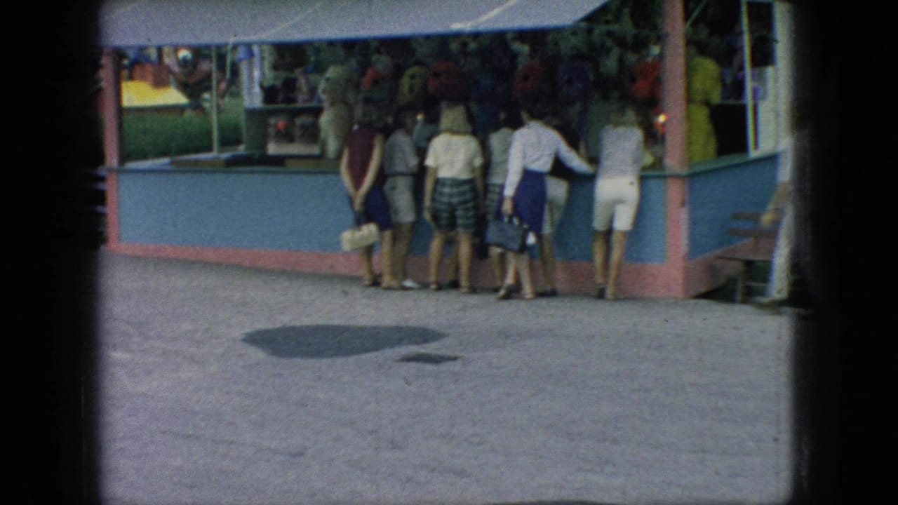 A small group of fair visitors stands at a pastel concession booth under an awning in 1966 New Jersey home-movie footage.