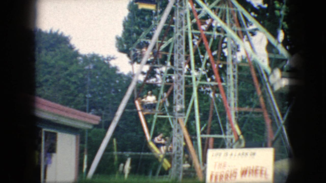 A small Ferris wheel with riders is visible beside trees and a fairground booth in New Jersey 1966 home-movie footage.