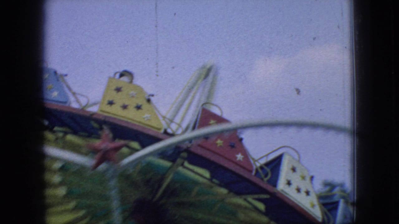 1966 New Jersey 8mm frame showing red and yellow star-decorated carnival swing cars moving past white curved rails and a pale sky.