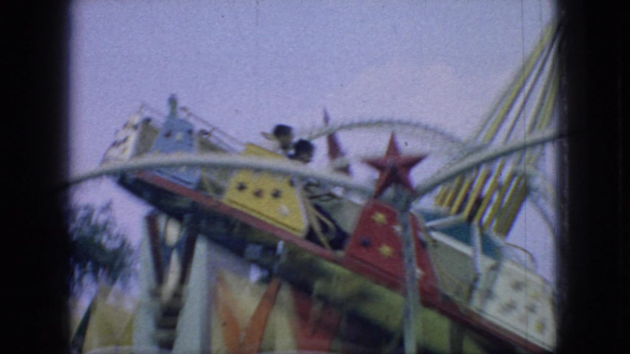 1966 New Jersey home-movie frame of a colorful carnival swing ride, with star-painted cars, white framework, and striped canopy elements visible in motion.