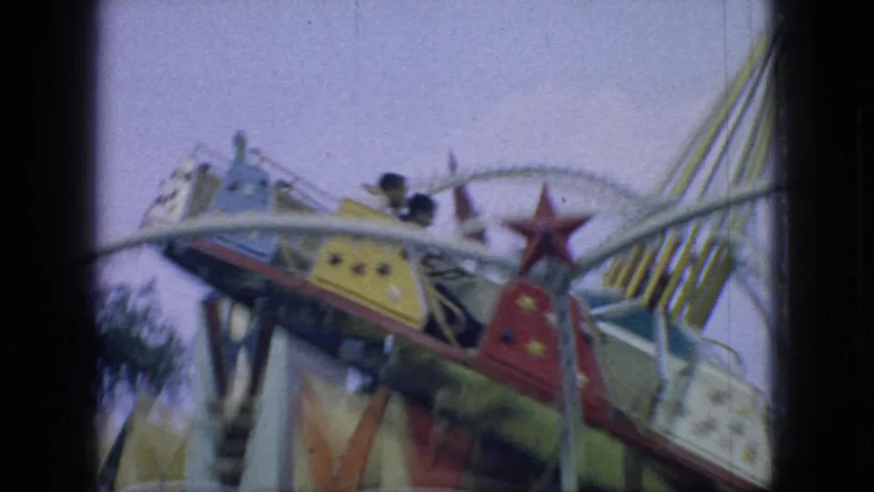 1966 New Jersey home-movie frame of a colorful carnival swing ride, with star-painted cars, white framework, and striped canopy elements visible in motion.