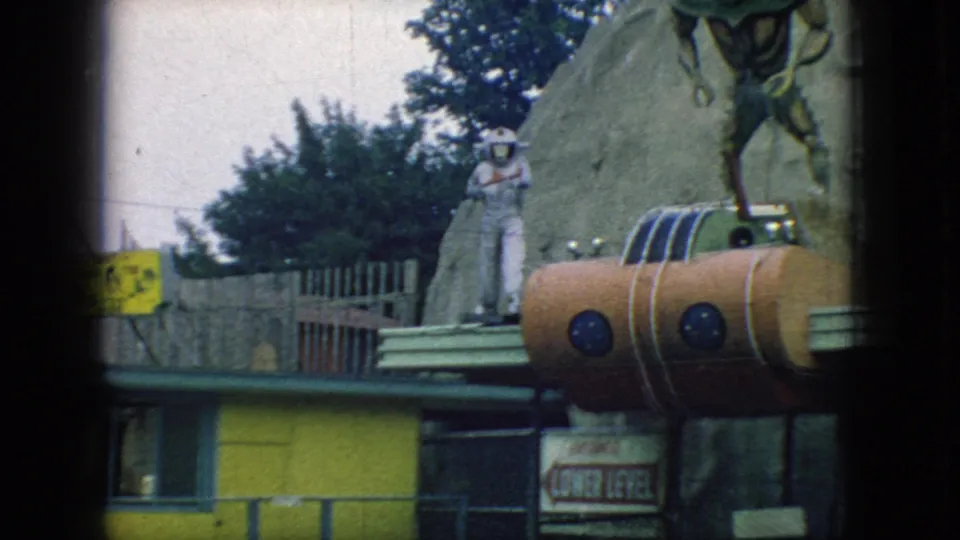 1966 New Jersey frame with a partial alien figure, a white astronaut figure, orange rocket-like attraction details, yellow building trim, and partially readable signage.