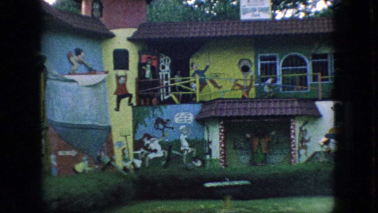 1966 New Jersey home-movie frame of a whimsical painted facade with bright yellow and green walls, animal and figure murals, arched windows, and landscaped foreground.