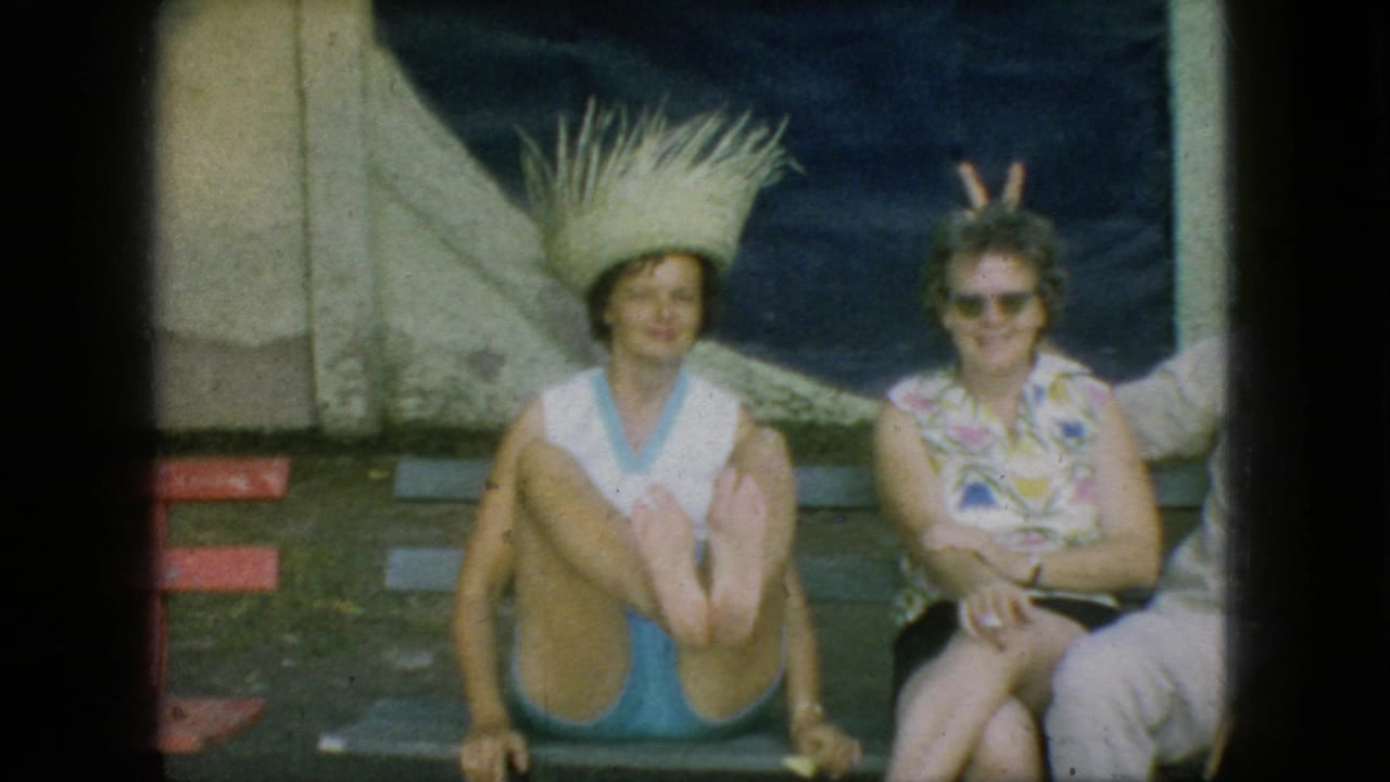 1966 New Jersey 8mm frame showing two women seated outdoors in a garden, with one in a large straw hat and another in a floral blouse and sunglasses.