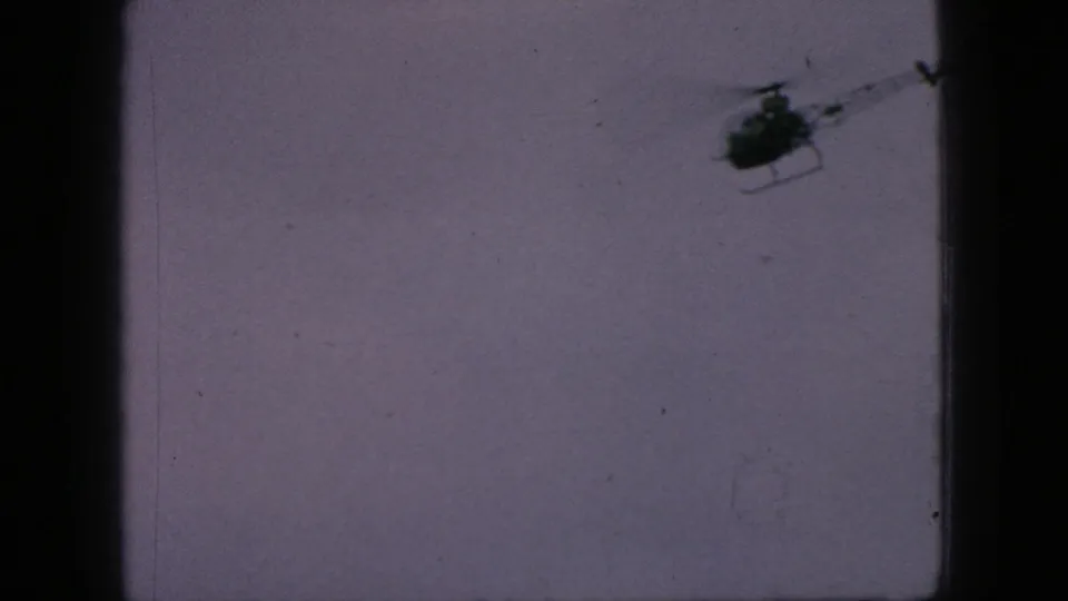 The helicopter nears the edge of the frame against the pale sky, with soft focus, faded color, and visible 8mm frame borders.
