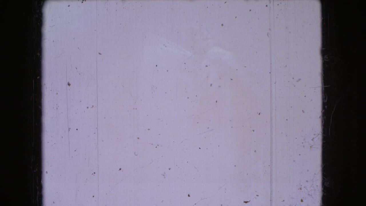 A mostly blank 8mm frame from the 1966 Ohio home-movie clip, showing pale exposure, dust specks, vertical scratches, and dark rounded frame edges.