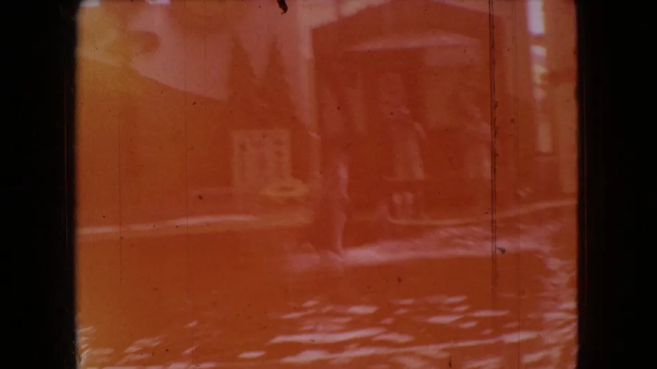 An orange-faded 8mm frame from the 1966 Ohio home-movie clip, showing rippled water, faint structural shapes, and an indistinct figure-like or marine-animal form.