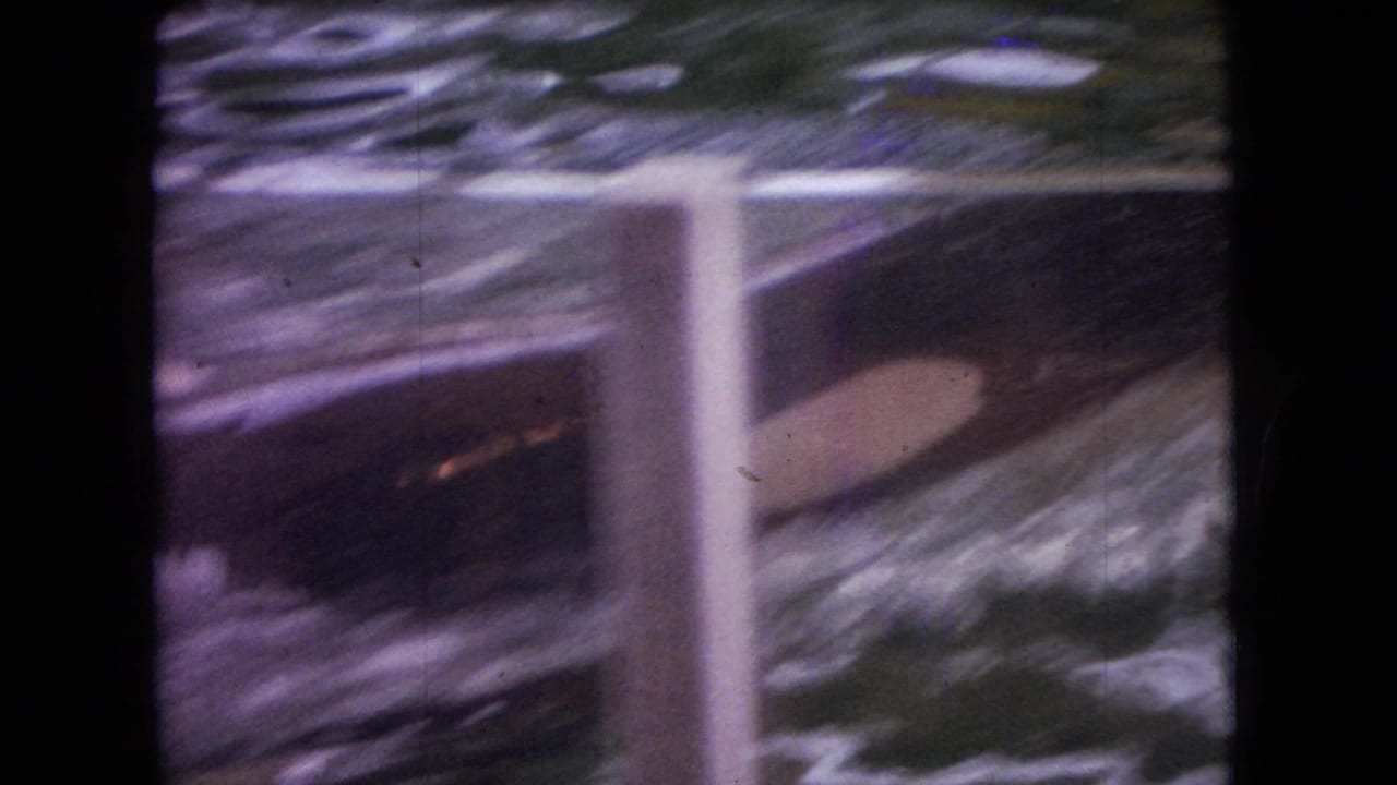 Faded 1966 Ohio 8mm frame showing a water-tank attraction through a barrier, with blurred rippling water, splashes, and vertical posts visible.