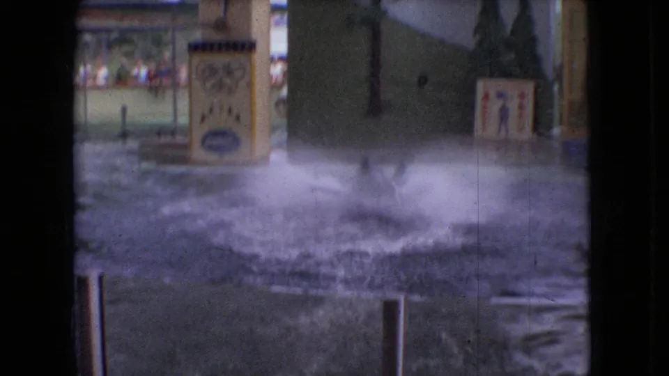 1966 Ohio aquarium-show frame showing a large splash in the performance pool, with painted signage, barriers, and spectators faintly visible in the background.