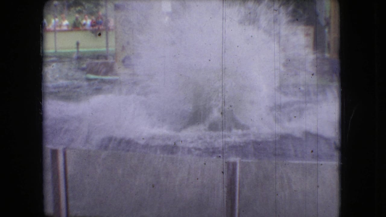 A 1966 Ohio 8mm frame shows spray rising from an aquarium performance pool, with railings, signage, and distant spectators visible in the background.