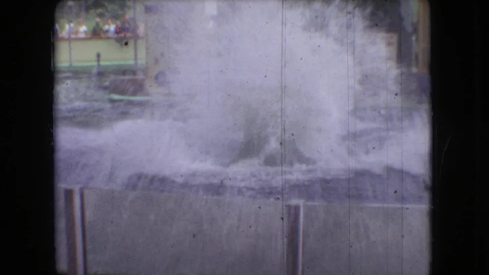 A 1966 Ohio 8mm frame shows spray rising from an aquarium performance pool, with railings, signage, and distant spectators visible in the background.