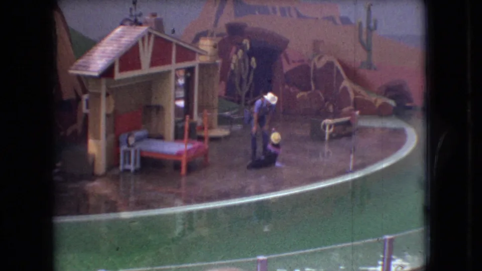 1966 Ohio 8mm frame with the performer and seal near the center of a wet performance ring, backed by a small house prop and painted desert scenery.