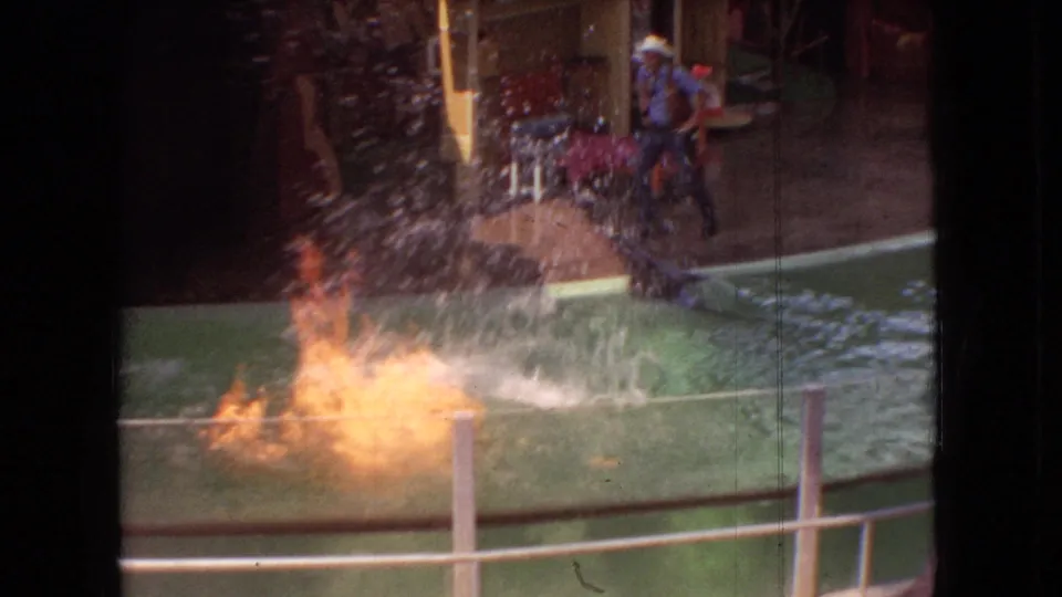 1966 Ohio 8mm frame showing a dark sea lion creating a large splash in a green show pool while spectators sit near the platform.