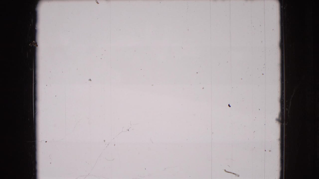 Mostly blank or overexposed 8mm frame with dark film borders, small dust specks, vertical scratches, and no clear subject visible.