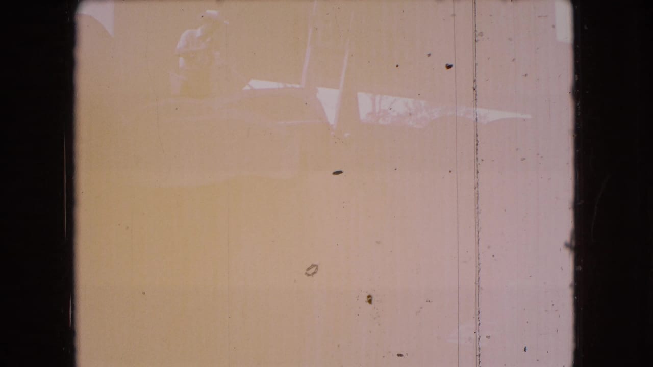 Tinted 8mm frame with dark borders, dust, vertical scratches, and faint indistinct forms without a clearly identifiable subject.