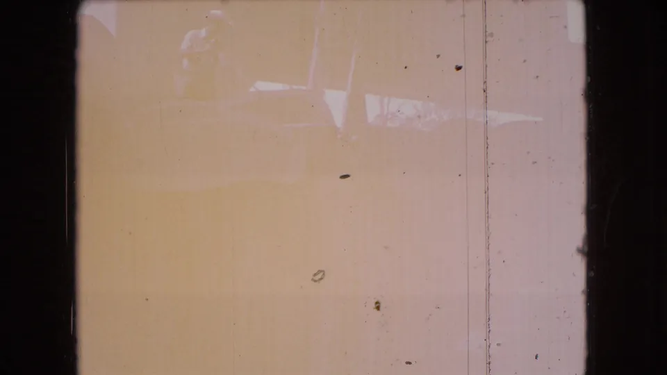 Tinted 8mm frame with dark borders, dust, vertical scratches, and faint indistinct forms without a clearly identifiable subject.