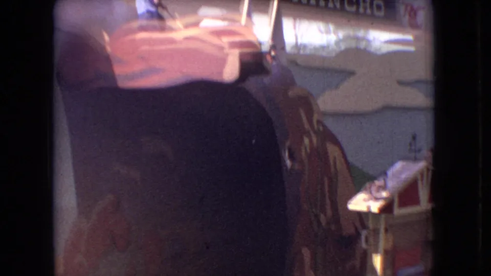 1966 Ohio 8mm frame showing a visitor's view of a man-made theater attraction with painted cliff scenery, partial signage, and an audience member's head at the bottom edge.