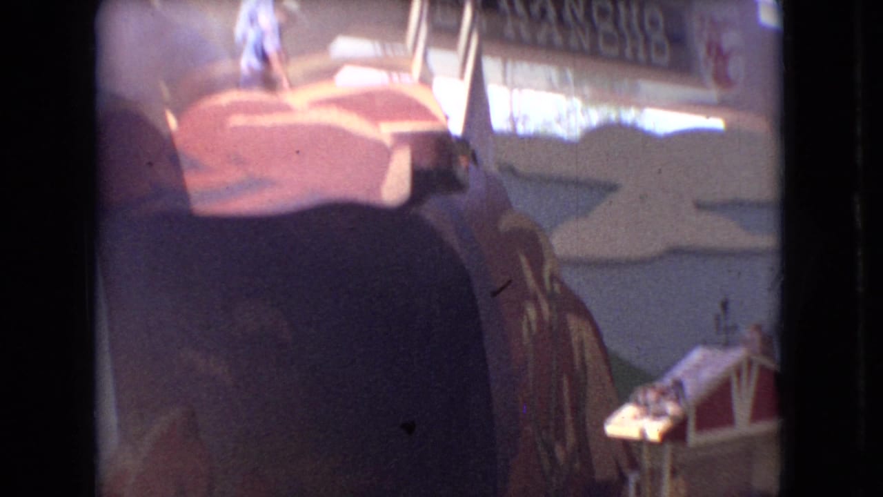 Similar audience view of the attraction set with a man on the upper painted structure and partial signage behind him.