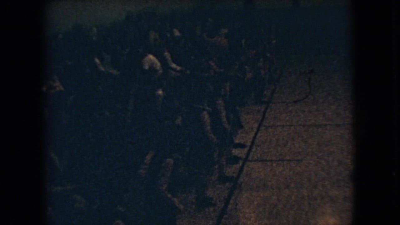 1966 Ohio 8mm frame showing a dim, crowded indoor gathering from above, with mostly silhouetted people standing and moving near a patch of floor.