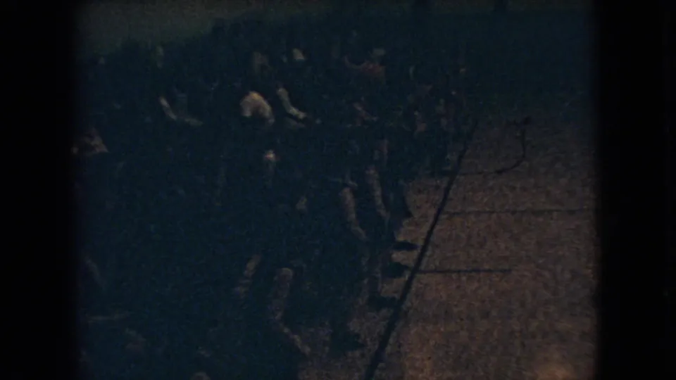 1966 Ohio 8mm frame showing a dim, crowded indoor gathering from above, with mostly silhouetted people standing and moving near a patch of floor.